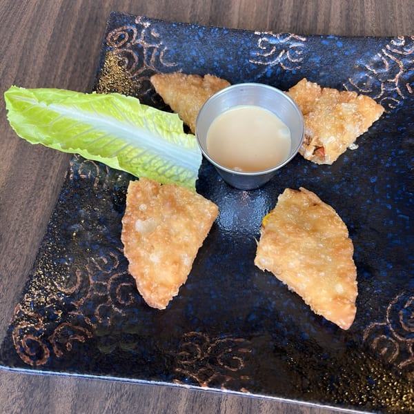 Four golden-fried wontons and a side of sauce on a dark blue plate with a lettuce leaf.