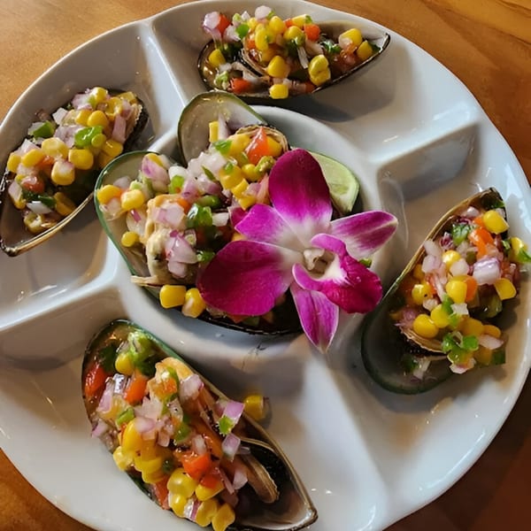 Peruvian mussels topped with corn, red onion, and peppers, garnished with an orchid and lime.