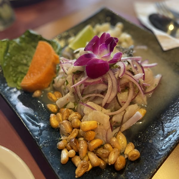 Peruvian ceviche with fish, red onions, sweet potato, corn, and a purple orchid garnish.