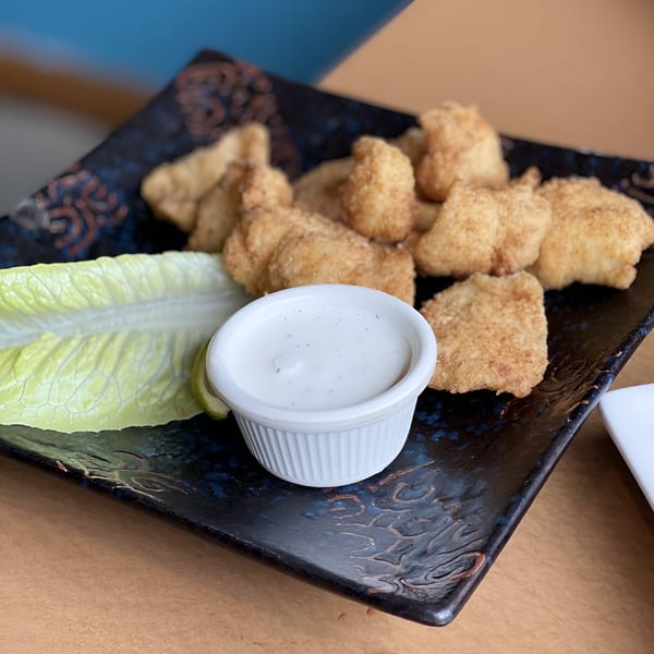 Crispy Peruvian chicken bites with a side of ranch dressing and lettuce on a dark plate.