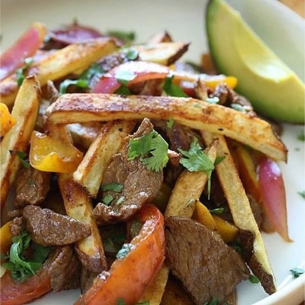 Peruvian Lomo Saltado with steak, fries, peppers, onions, cilantro, and a side of avocado.