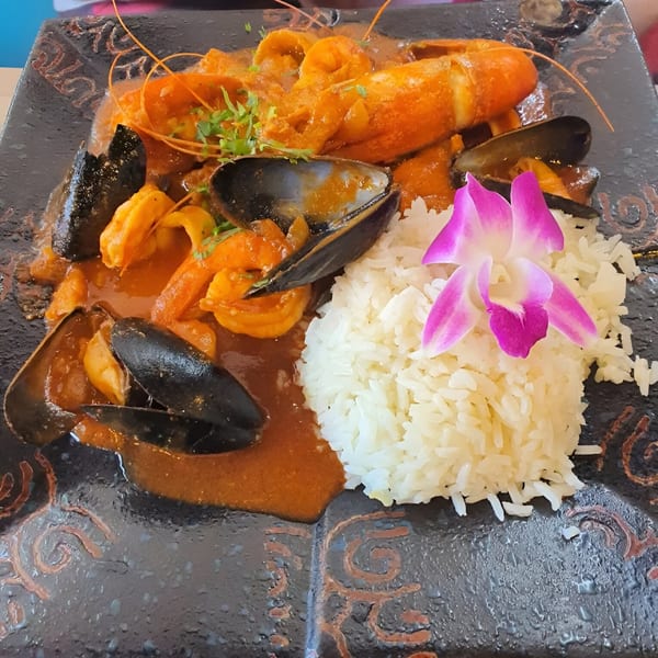 Peruvian seafood dish with lobster, mussels, shrimp, and rice, garnished with a purple orchid.